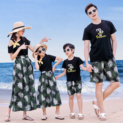 Family of four in matching black and green tropical print outfits on a beach, featuring t-shirts, shorts, skirt, and wide-leg pants. - Image 5