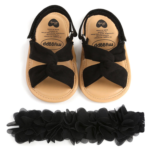 Black baby sandals with knotted cross straps and a matching black floral headband on a white background. - Image 12