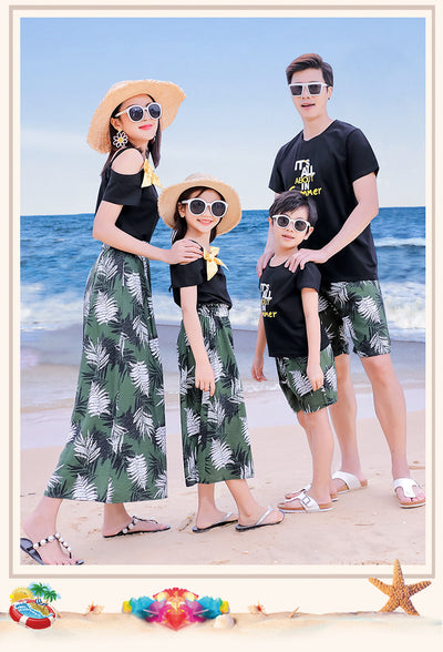 Family of four in matching black and green tropical print outfits on a beach, featuring t-shirts, shorts, skirt, and wide-leg pants. - Image 14