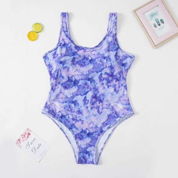 Purple tie-dye one-piece swimsuit with a scoop neck, worn by a person in a poolside setting.