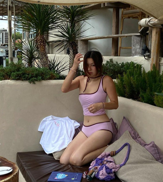 Women's light purple one-shoulder swimsuit with dark red contrast trim, lying on a striped blanket on green grass. - Image 28