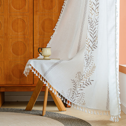 White semi-sheer curtain with brown botanical embroidery and white tassels, draped over a small wooden table. - Image 9