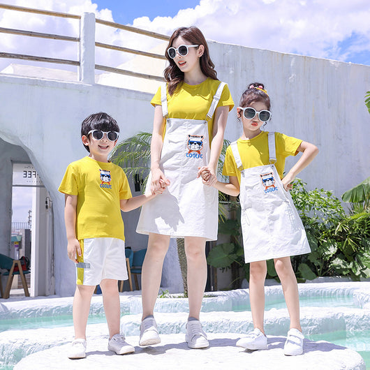 Family of three in matching yellow t-shirts and white outfits by a pool. Father and son wear shorts, mother and daughter wear overall dresses. - Image 3