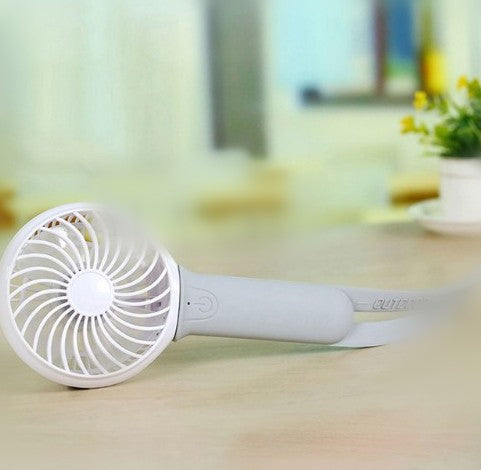 Lime green and white mini USB portable fan with a flexible strap, lying on a light wooden surface. - Image 6
