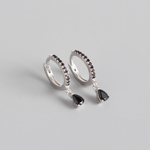 Silver-colored hoop earrings with black pave stones and dangling black teardrop-shaped stones.