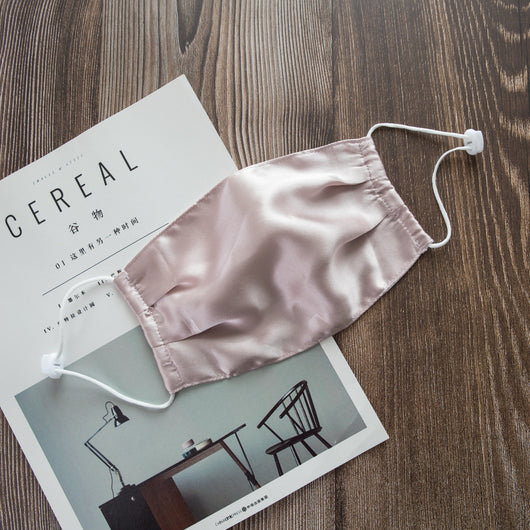 Light pink double layer silk face mask with adjustable white ear loops on an open magazine.