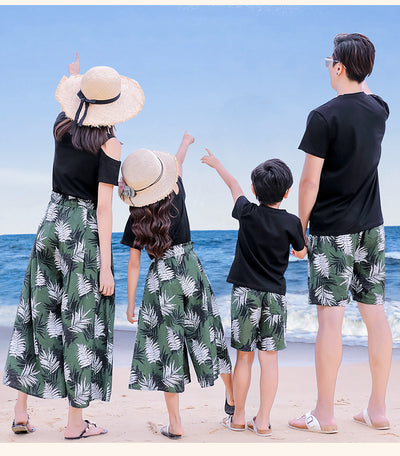 Family of four in matching black and green tropical print outfits on a beach, featuring t-shirts, shorts, skirt, and wide-leg pants. - Image 15
