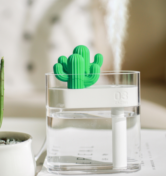Transparent portable humidifier with a green cactus design on top, emitting mist on a wooden desk next to a laptop. - Image 13