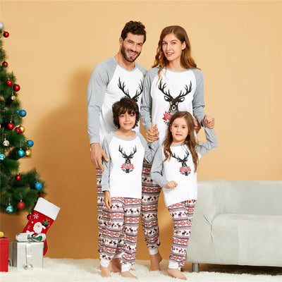 Young boy wearing a Christmas pajama set with a white and grey raglan top featuring a reindeer and fair isle print pants.