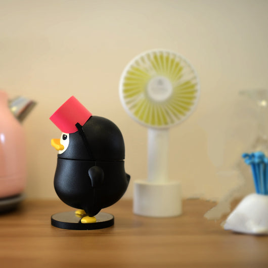 Black diving duck spray humidifier with red goggles and yellow feet, standing on a dark base on a table. - Image 6