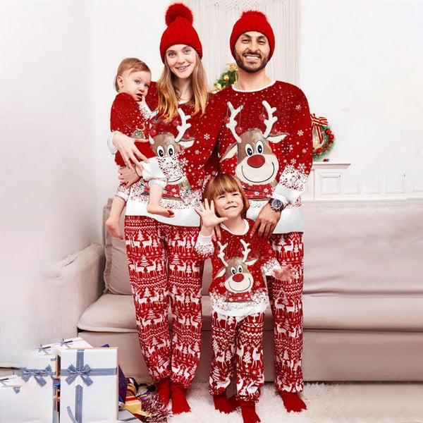 Family of four wearing matching red Christmas pajamas with reindeer and snowflake patterns and red pom-pom beanies.