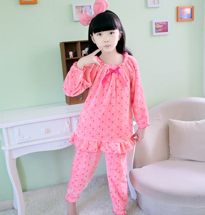 Young woman wearing a pink coral fleece thermal pajama set with white and red polka dots and ruffled hems.