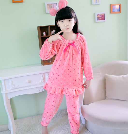 Young woman wearing a pink coral fleece thermal pajama set with white and red polka dots and ruffled hems.