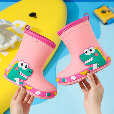 Bright yellow children's rain boots with a green cartoon dinosaur design and orange trim, held by hands. - Image 11