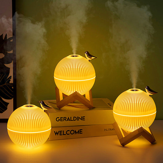 White spherical humidifier with ribbed texture, warm glow, metallic bird accent, and light brown wooden stand. - Image 10