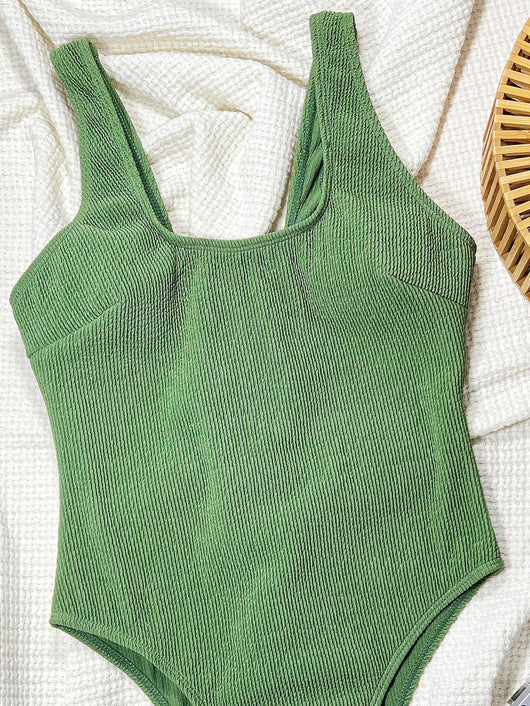 Woman wearing a ribbed sage green one-piece swimsuit with a scoop neck and high-cut leg, sitting on a lounge chair. - Image 7