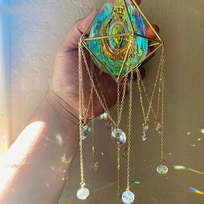 Geometric iridescent suncatcher with a gold frame and dangling crystal pendants, held in a hand, creating rainbow light. - Image 9