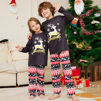 Two children wearing black long-sleeve Christmas pajamas with a "Merry Christmas" reindeer design and fair isle pants.