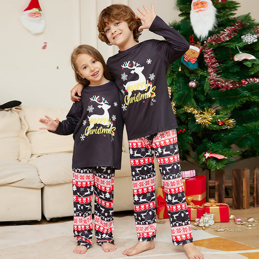Two children wearing black long-sleeve Christmas pajamas with a "Merry Christmas" reindeer design and fair isle pants.