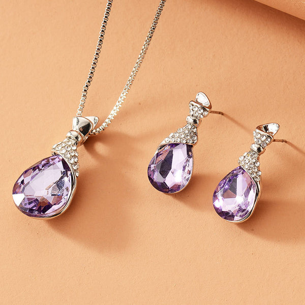 Rose gold tone bridal jewelry set with a necklace and stud earrings, each featuring a large blue teardrop gem and clear accents.