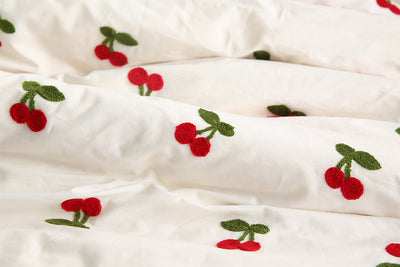 White pure cotton fabric with embroidered red cherries and green leaves, draped to show texture. - Image 4