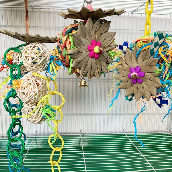 Colorful parrot chew toy made from natural fibers, featuring a woven ball, leaf-like accents, a bell, and a carabiner clip.