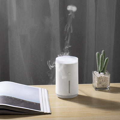 Porcelain white cylindrical humidifier emitting jellyfish-shaped mist, sitting on a round base against a split teal and dark green background.