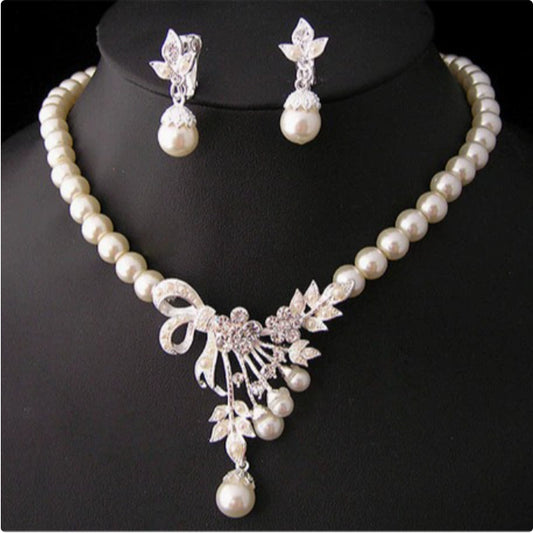 Elegant pearl necklace and matching drop earrings set with rhinestone bow and floral accents, ideal for bridal wear.