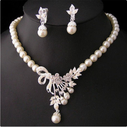 Elegant pearl necklace and matching drop earrings set with rhinestone bow and floral accents, ideal for bridal wear.