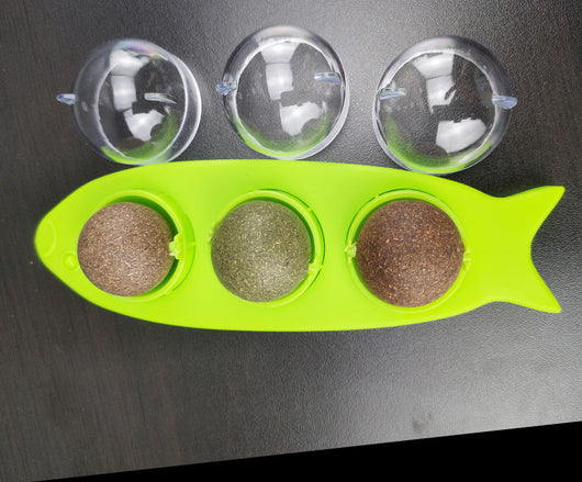 Pink fish-shaped cat molar stick toy with three compartments holding green and brown catnip or silvervine balls. Three clear plastic dome covers are shown. - Image 12