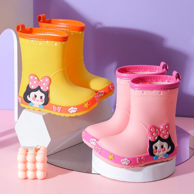 Bright yellow children's rain boots with a green cartoon dinosaur design and orange trim, held by hands. - Image 2