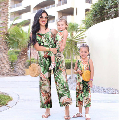 Mother and two daughters in matching green tropical print jumpsuits, posing outdoors in a sunny resort setting. - Image 9