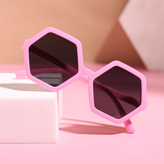 Red hexagonal children's sunglasses with dark lenses on a pink surface with a white block. - Image 9