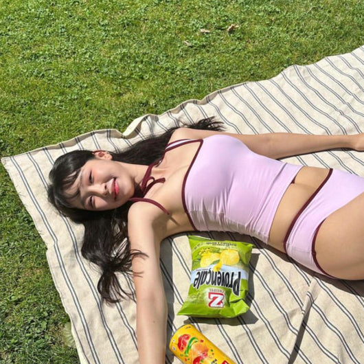 Women's light purple one-shoulder swimsuit with dark red contrast trim, lying on a striped blanket on green grass. - Image 4