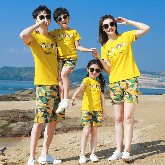 Family of four wearing matching yellow short-sleeved t-shirts with 'HAPPY DAY!' and geometric print shorts on a beach. - Image 2