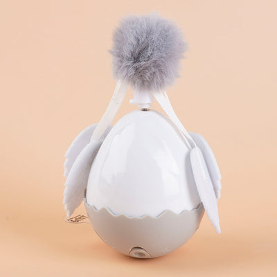 Electronic cat motion toy, a white and grey tumbler ball with fluffy pom-pom and soft wings, next to its retail box. - Image 8