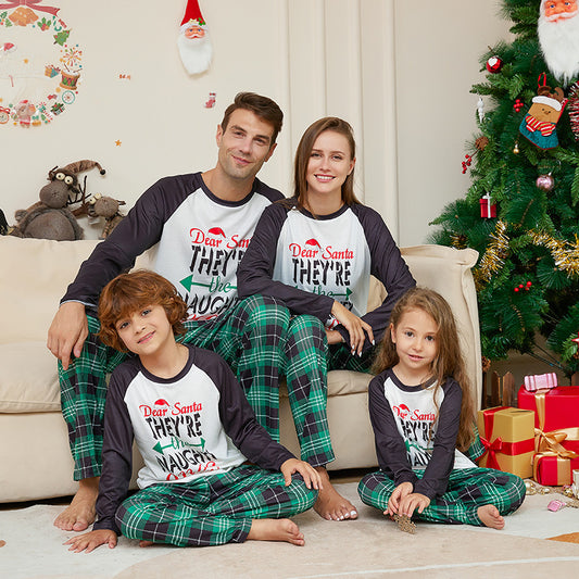 Man wearing a white and black raglan long-sleeve pajama top with a 'Dear Santa They're the Naughty Ones' graphic and green plaid pajama pants.