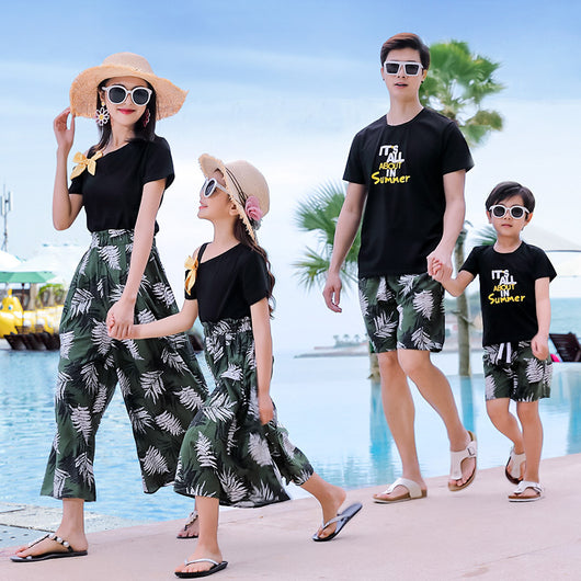 Family of four in matching black and green tropical print outfits on a beach, featuring t-shirts, shorts, skirt, and wide-leg pants. - Image 19