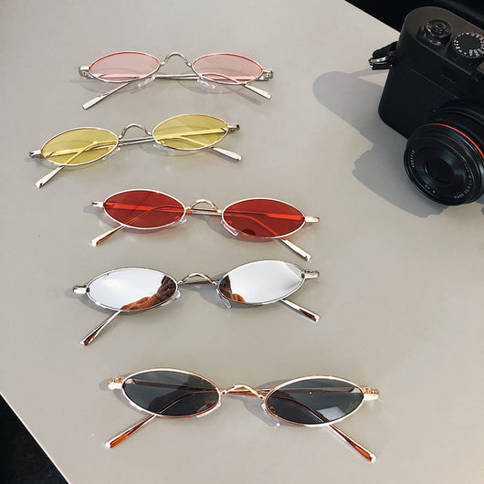 Silver-framed oval sunglasses with dark lenses reflecting a warm-toned object, displayed on a white tray.