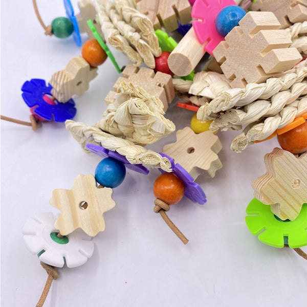 Colorful parrot gnawing toy with wooden blocks, woven straw, and plastic beads, hanging from a metal hook.