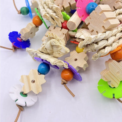 Colorful parrot gnawing toy with wooden blocks, woven straw, and plastic beads, hanging from a metal hook.