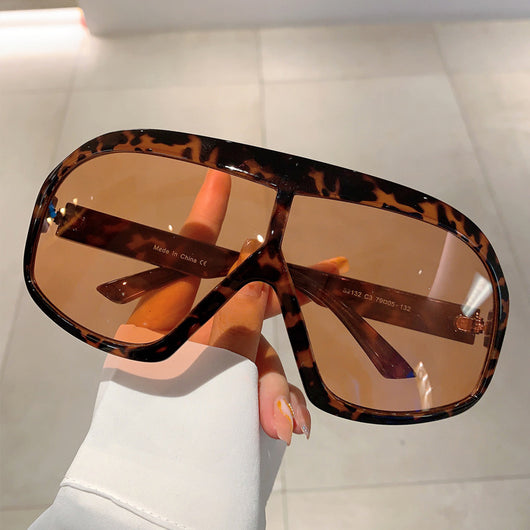 Oversized women's shield sunglasses with a tortoiseshell frame and brown-tinted lenses, held by a hand. - Image 16