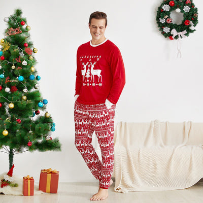 Family of four wearing matching red Christmas pajamas with white reindeer and tree patterns, standing by a decorated tree. - Image 5