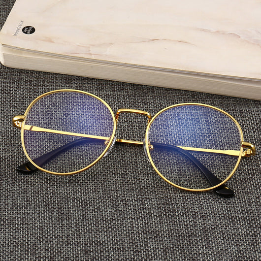 Gold round-frame anti-blue light glasses with clear resin lenses on a gray textured surface next to a notebook. - Image 2
