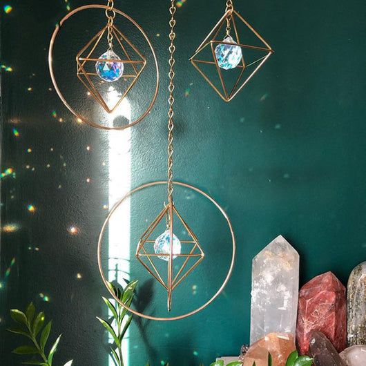 Geometric iridescent suncatcher with a gold frame and dangling crystal pendants, held in a hand, creating rainbow light. - Image 13