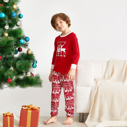 Family of four wearing matching red Christmas pajamas with white reindeer and tree patterns, standing by a decorated tree. - Image 3