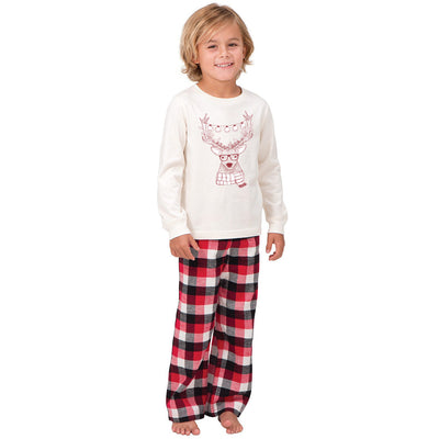 Child wearing a cream long-sleeve pajama top with a reindeer graphic and red, black, and white plaid pajama pants. - Image 2