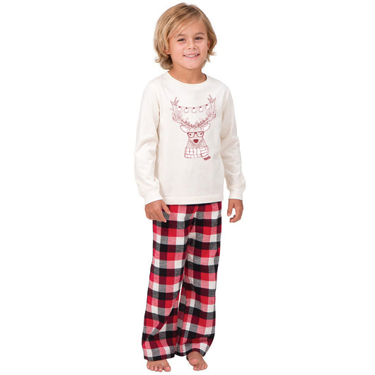Child wearing a cream long-sleeve pajama top with a reindeer graphic and red, black, and white plaid pajama pants. - Image 2