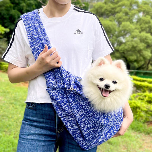 Person in white hoodie carrying a happy white dog in a navy blue pet sling bag outdoors. - Image 49