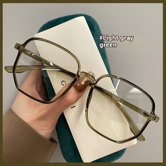 Mocha brown irregular frame glasses with clear lenses, held over a dark green velvet glasses case. - Image 6
